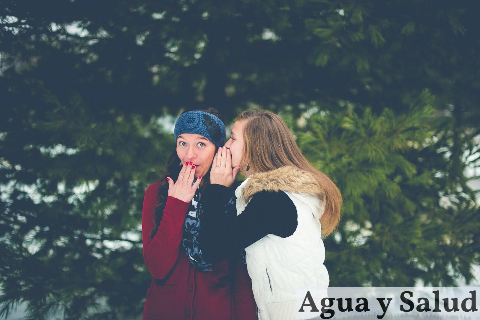 woman whispering on woman's ear while hands on lips
