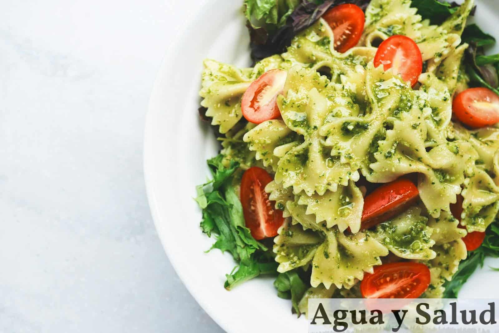 Pesto pasta with sliced tomatoes served on white ceramic plate