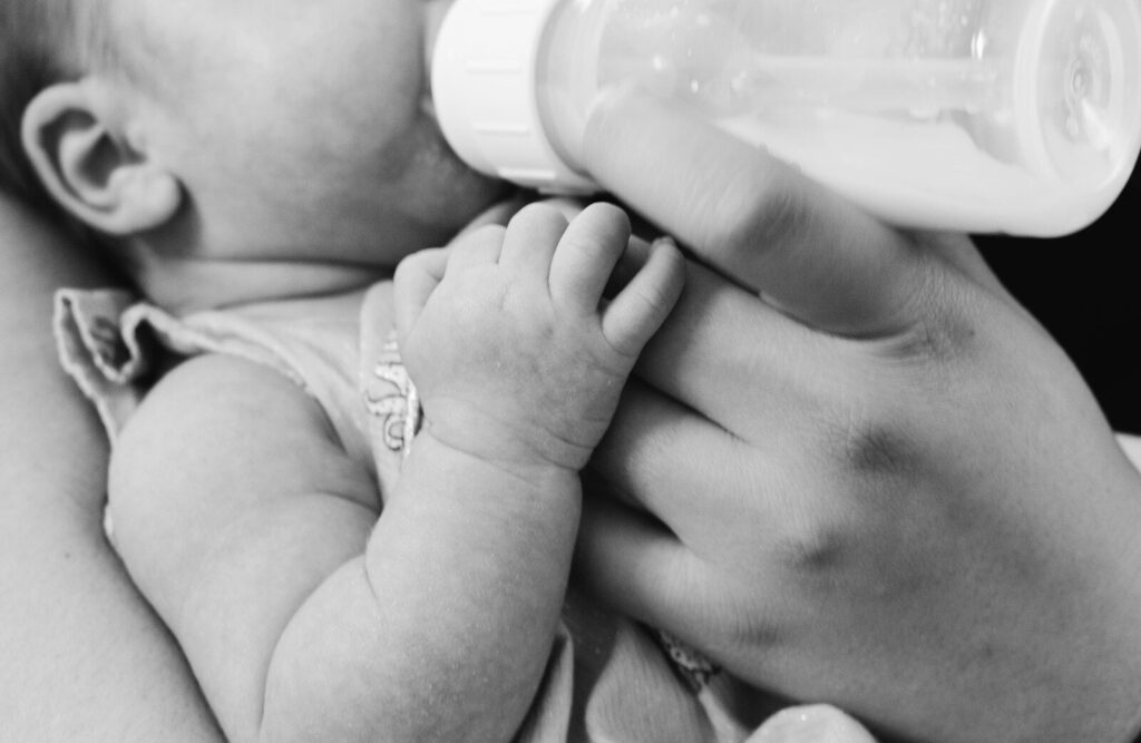 Manos de un bebé agarrando el biberón en blanco y negro